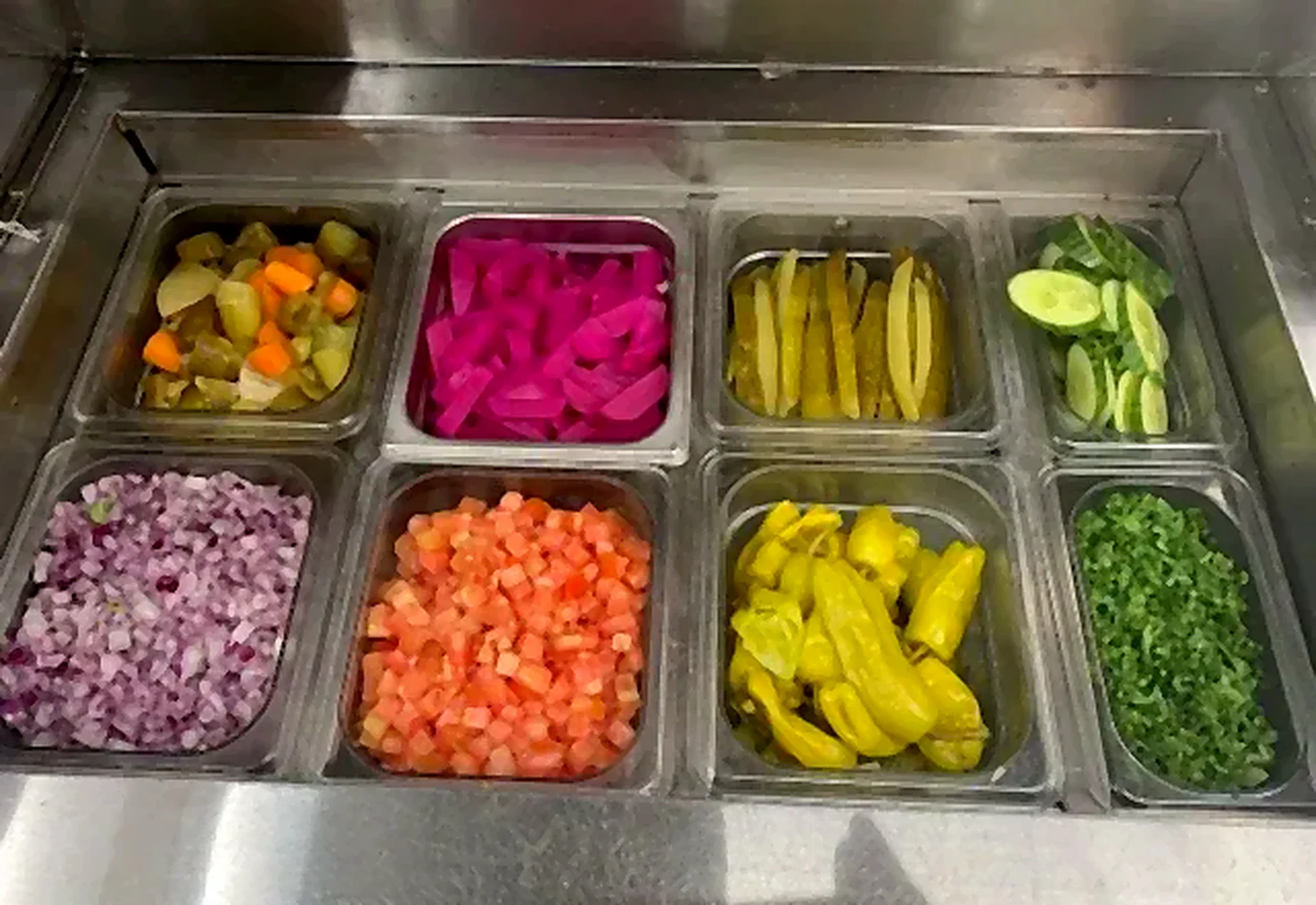 Prep station with pickles, peppers, onions, tomatoes and herbs
