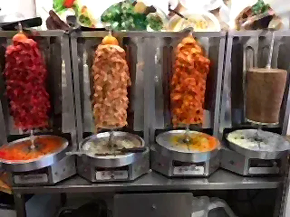 Row of vertical shawarma spits with sauces